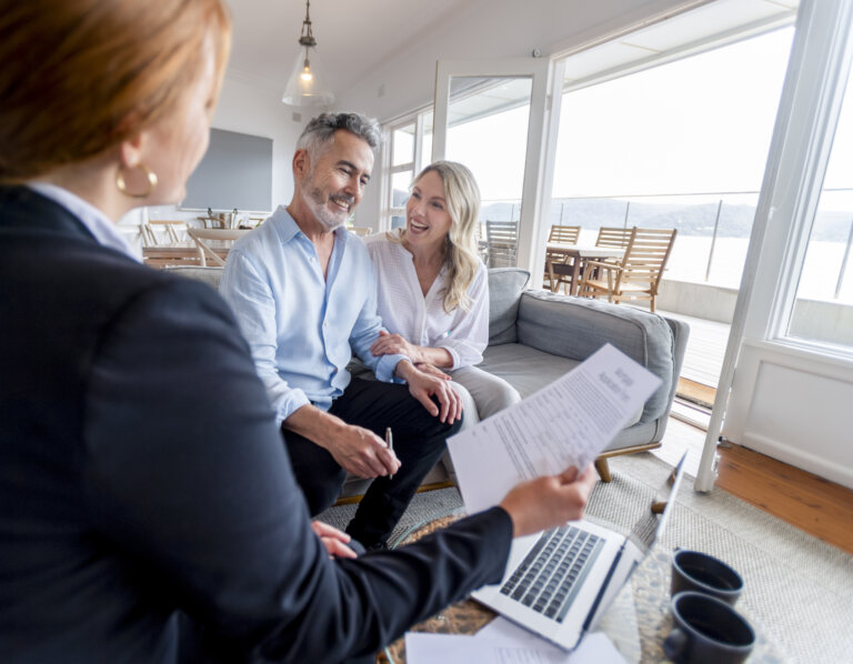 Happy mature couple meeting investments and financial advisor at home. They are happy and smiling sitting in the living room. The advisor is holding a document. There is a laptop on the table